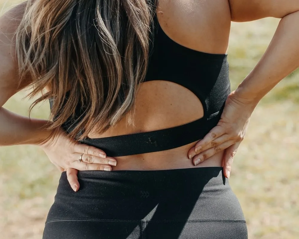 Donna in abbigliamento sportivo con le mani sulla zona lombare per il mal di schiena
